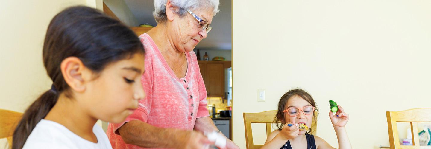 a grandmother feeds her grandchildren dinner