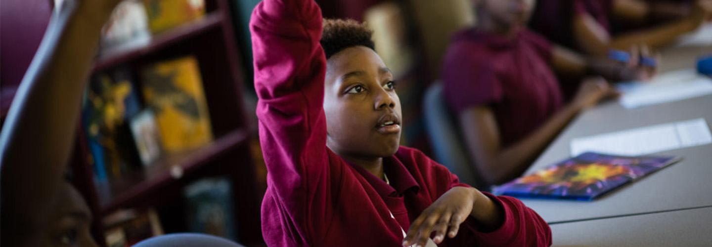 a young boy raises his hand in class