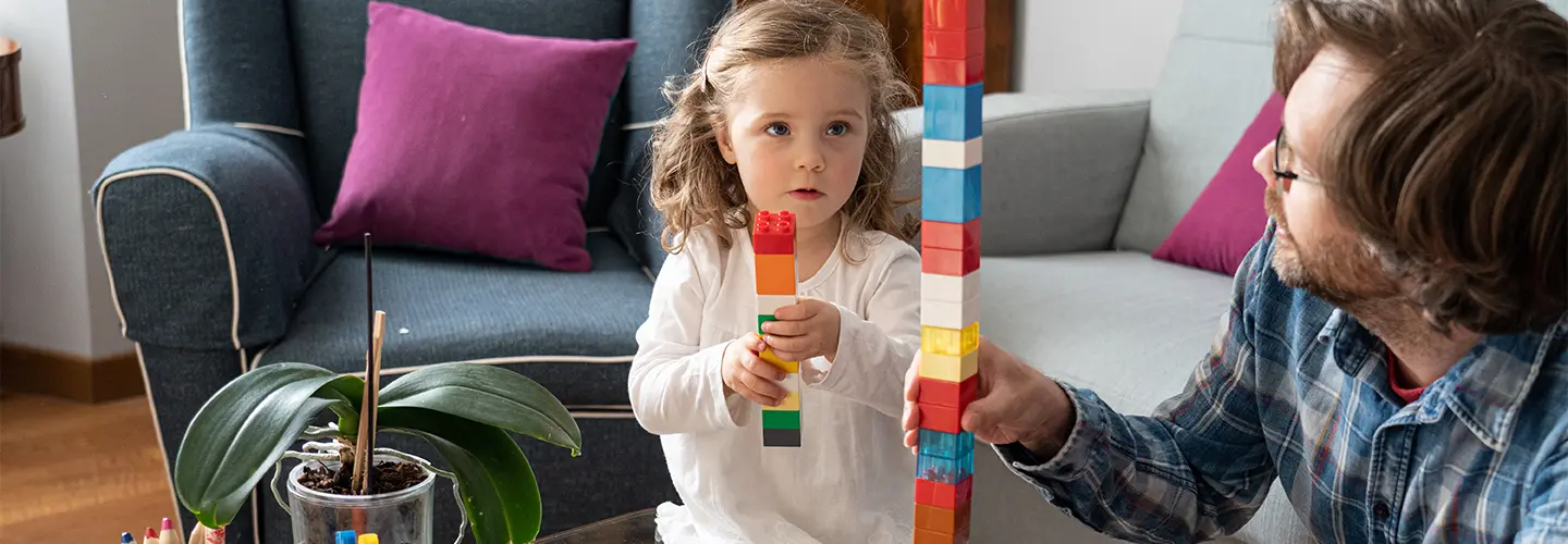 A young girl and man play with building blocks