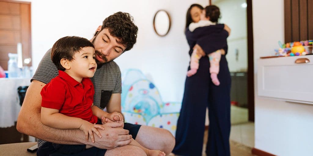 a father holds his young son, while a mother stands in the background
