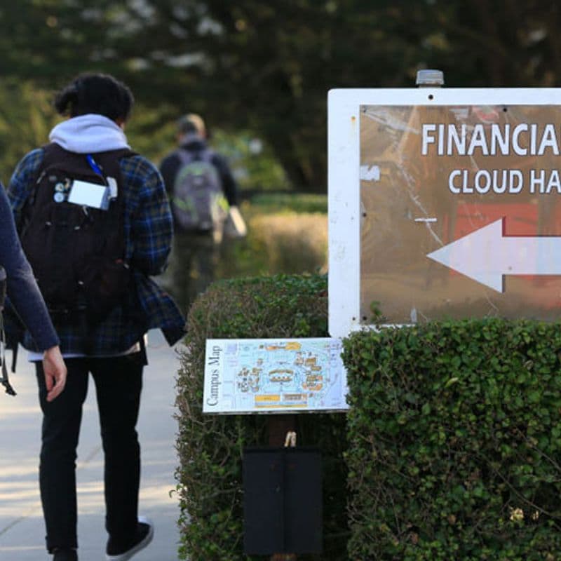 students walk past a sign for the school's financial aid office.
