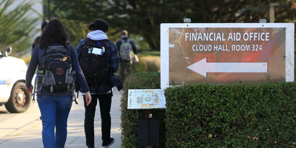 students walk past a sign for the school's financial aid office.